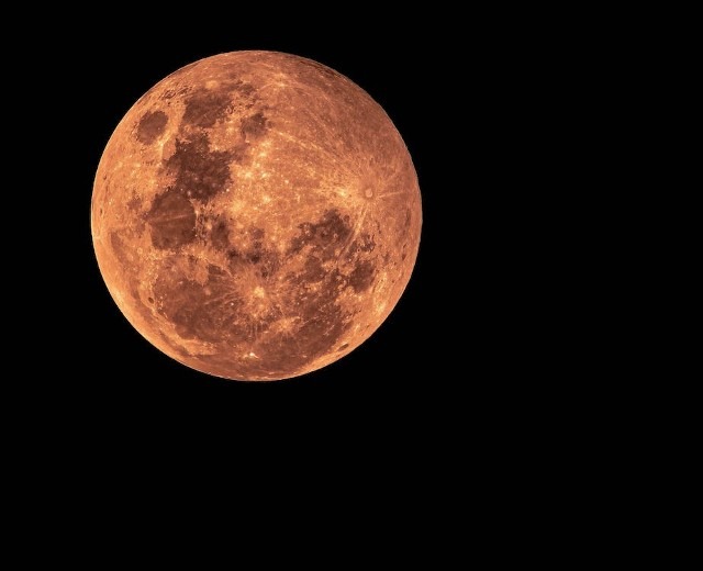 Bright orange full moon against a black background, showcasing its craters and textures, illustrating lunar beauty and wonder.