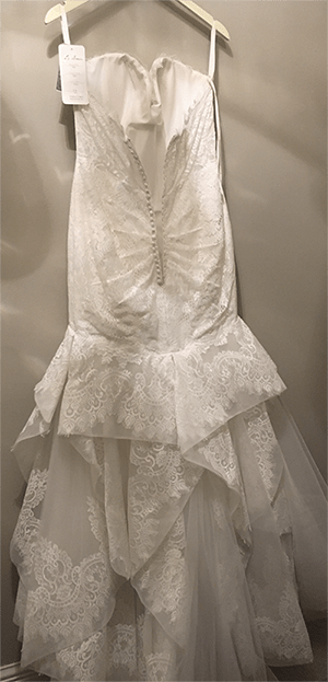 Elegant white wedding dress featuring intricate lace details and a layered skirt, displayed on a hanger in a fitting room.