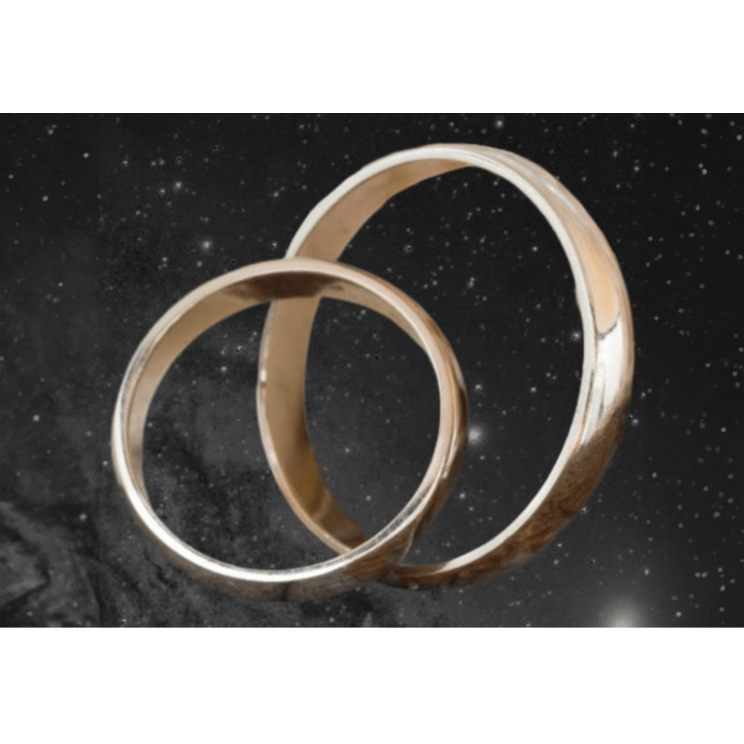 Two intricately designed metallic wedding bands float against a cosmic backdrop, symbolizing love and unity in an expansive universe.